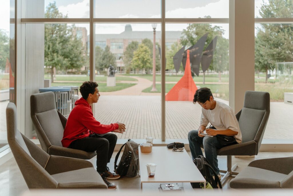Two students having lunch together next to large windows overlooking campus